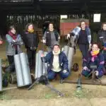 9 agricultrices du groupe femmes Les Elles posent face à l'objectif, devant une grange, avec des objets métalliques.