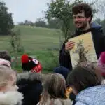 Un homme souriant montre un schéma à des enfants, au milieu d'un chantier de plantation.