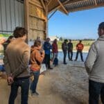 Un groupe d'agriculteurs est regroupé autour d'une femme en train de parler dans une grange ouverte