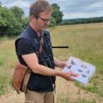 L'animateur de l'atelier biodiversité montre différentes espèces de papillons sur un livre, dans un champ